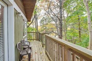 A wooden deck with chairs and a table, surrounded by trees.