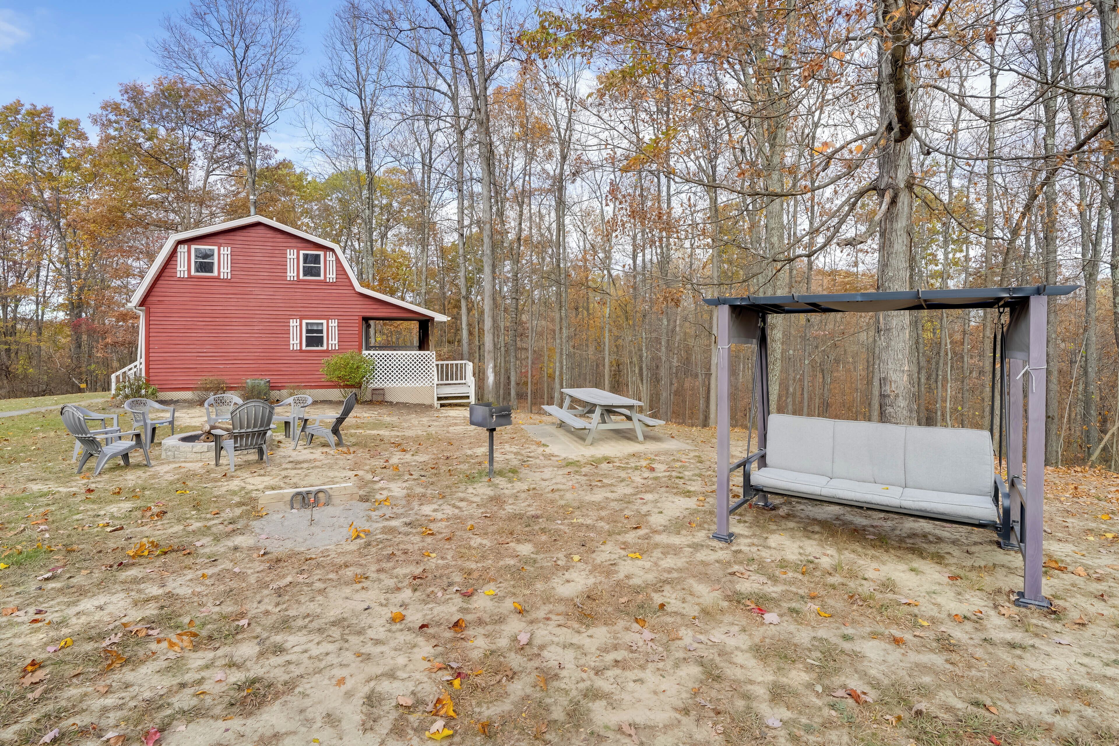 A red house with a deck, outdoor seating, and a swing set in a wooded area.