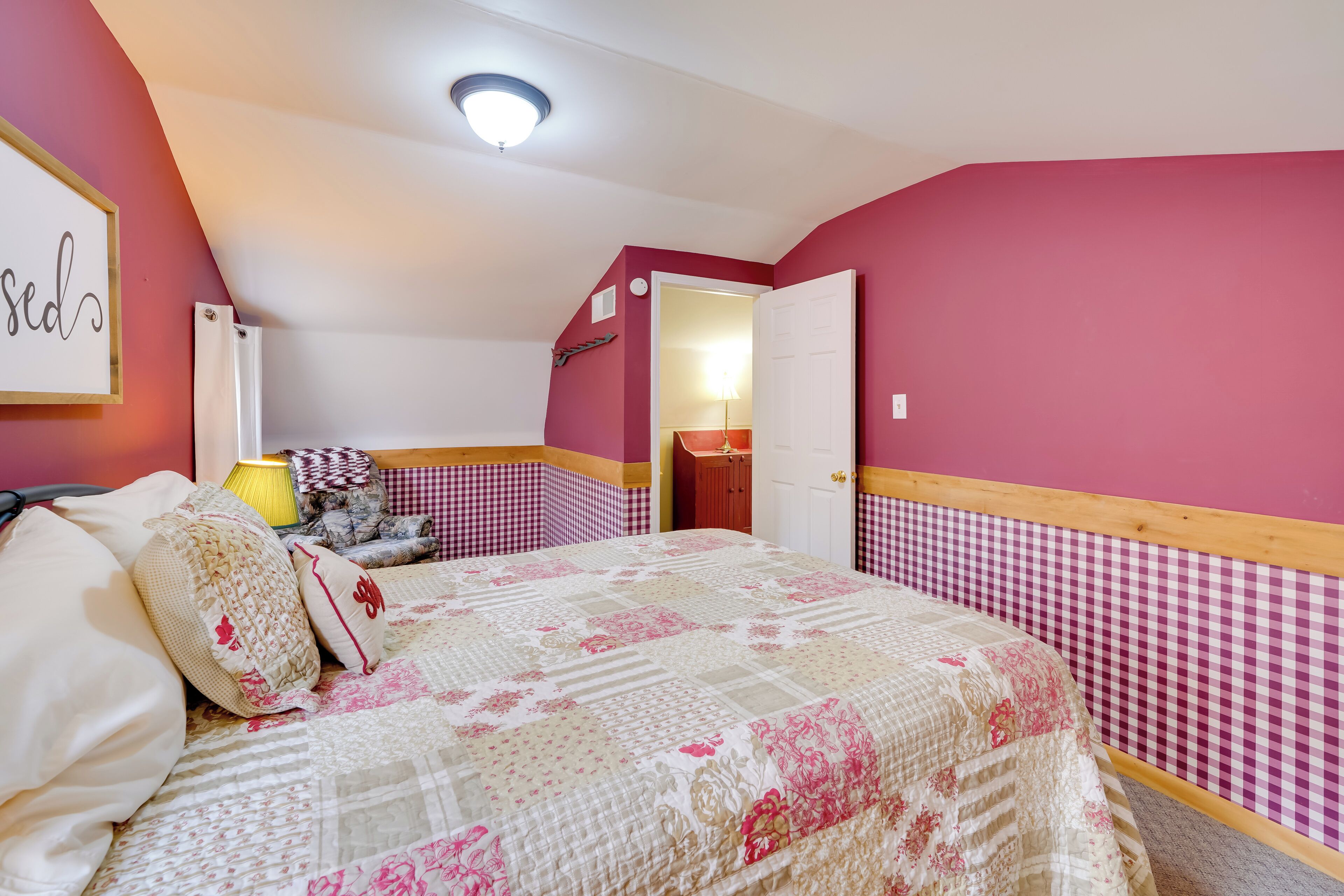 Un dormitorio con pared a cuadros, una cama con colcha floral y una puerta visible que da a otra habitación.