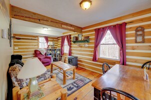 Un interior de cabaña acogedor con una mesa de comedor de madera, un sofá, una lámpara y una estantería.