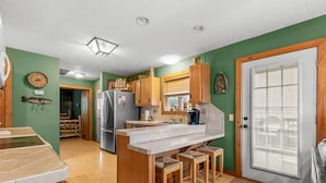Una cocina con armarios de madera, una isla central con taburetes, un refrigerador y un reloj en la pared.