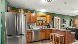 Una cocina con armarios de madera, electrodomésticos de acero inoxidable, una ventana con persianas y una pequeña isla con taburetes.