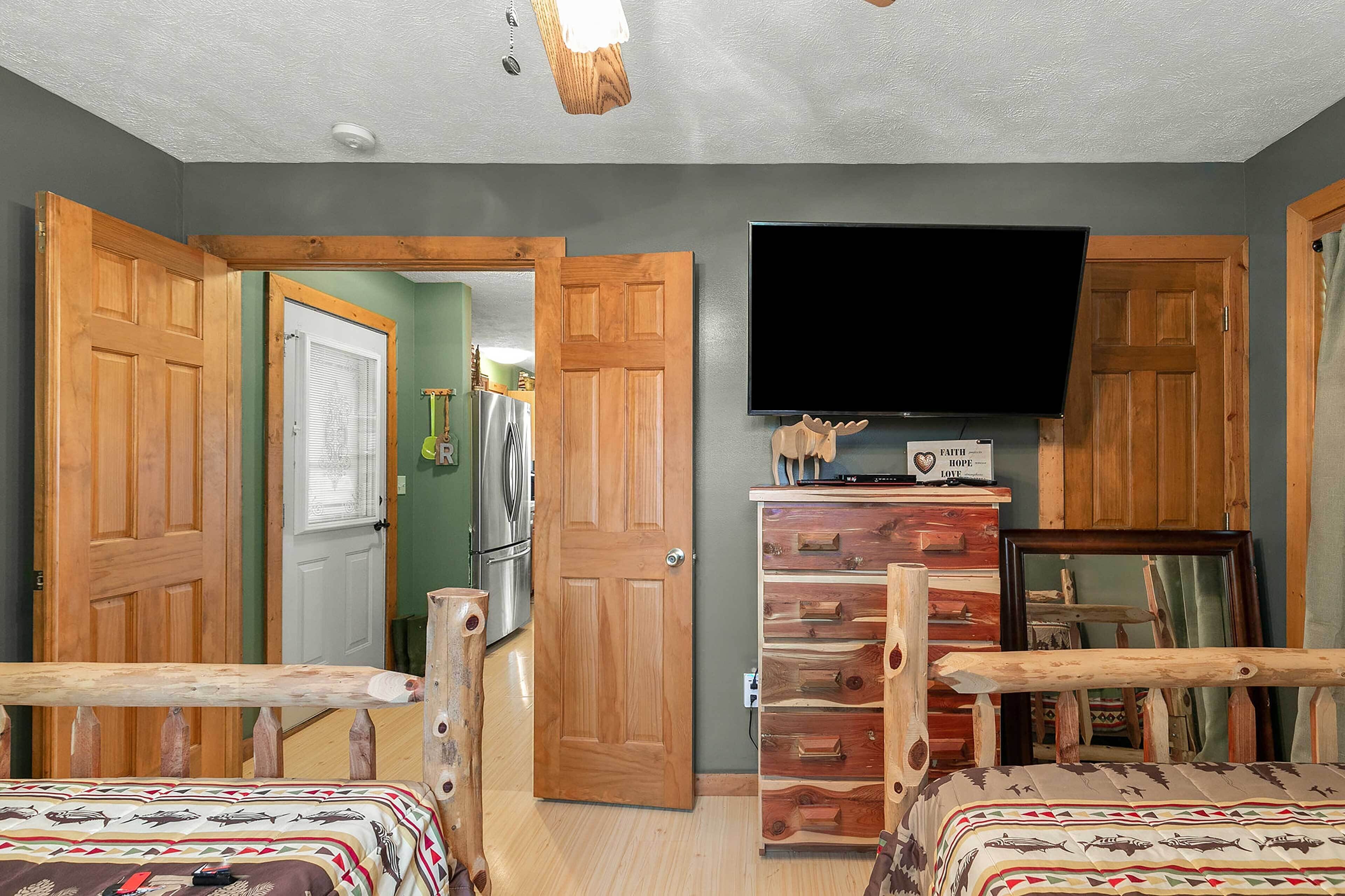 A room with two beds, a wooden dresser, a television, and a door leading to a kitchen.