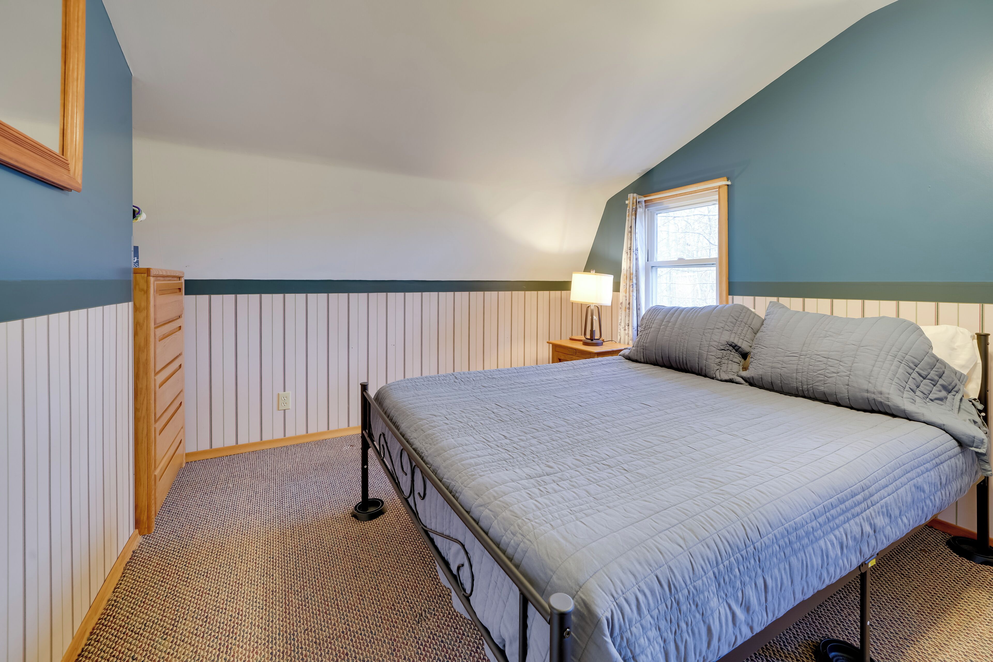Un dormitorio con cama, mesita de noche, lámpara y ventana.