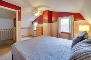 Un dormitorio con una cama grande, un ventilador de techo, un aparador y una ventana con cortinas.