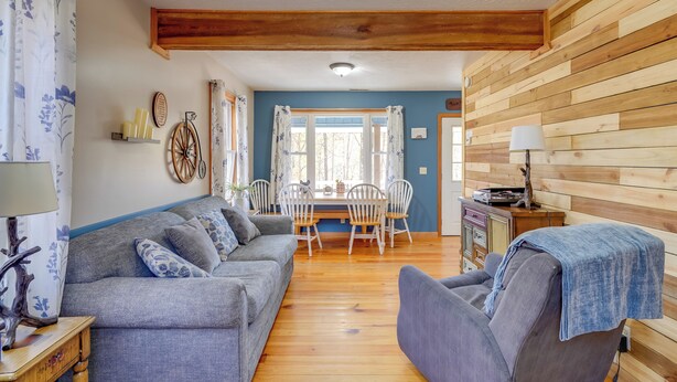 Ein gemütliches Wohnzimmer mit grauem Sofa, blauem Sessel, Holzboden und einer Essecke mit Tisch und Stühlen.