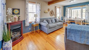 Ein gemütliches Wohnzimmer mit Kamin, einem grauen Sofa, Holzböden und einem Essbereich mit weißen Stühlen.