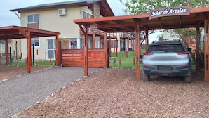 Une entrée fermée par un portail, avec une voiture garée sous une pergola en bois.