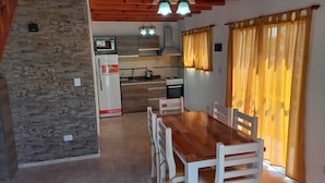 Un coin repas avec une table et des chaises en bois, une cuisine en arrière-plan et des rideaux jaunes.