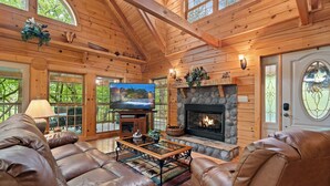 A log cabin interior with a fireplace, leather sofas, a television, and a stone fireplace surround. - Beautiful Three Bedroom Cabin Directly On Cosby Creek (Cosby)