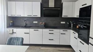 A modern kitchen with white cabinets, a black countertop, and a built-in oven. - Apartment on the edge of the Palatinate Forest. TLA/TDY (Ramstein-Miesenbach)