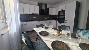 A modern kitchen with white cabinets, a black countertop, and a dining area with a white table set for six. - Apartment on the edge of the Palatinate Forest. TLA/TDY (Ramstein-Miesenbach)