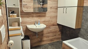 A modern bathroom with a wooden wall, a white sink, a toilet, and a bathtub. - Apartment on the edge of the Palatinate Forest. TLA/TDY (Ramstein-Miesenbach)