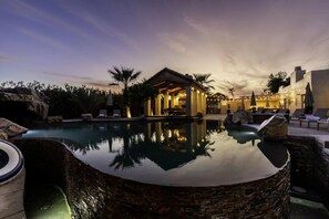 A pool area with a stone structure, lounge chairs, and a building with lights.