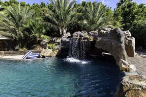 A clear pool with a waterfall feature surrounded by rocks and palm trees.