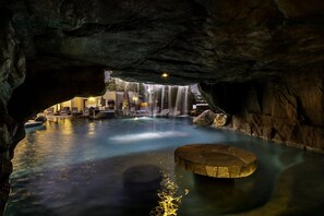 Een rustig binnenzwembad met een waterval, omringd door rotsformaties en een rond zitgedeelte.