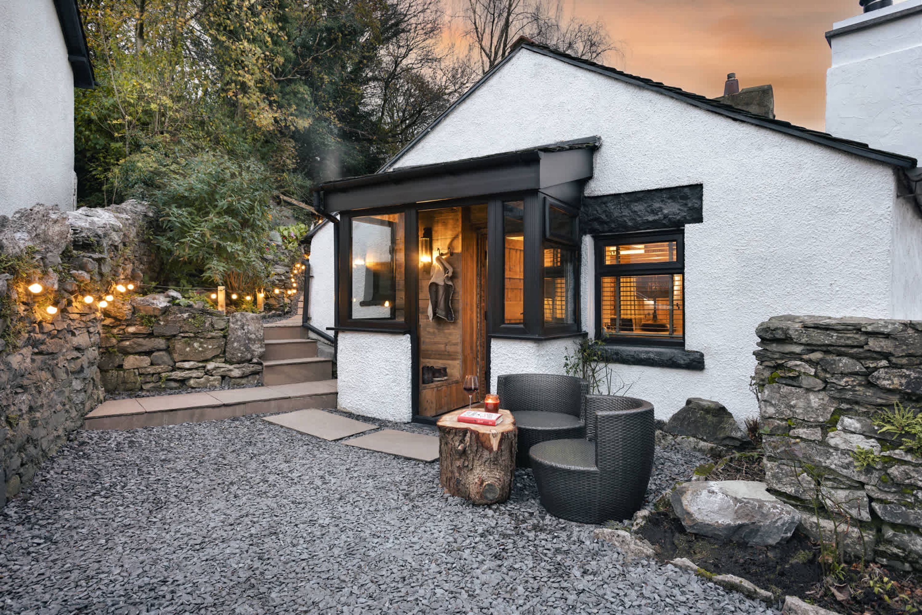 Una cabaña acogedora con fachada de piedra, puerta de madera y un área de estar con mesa y sillas.