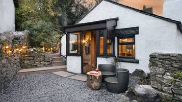 Una cabaña acogedora con fachada de piedra, puerta de madera y un área de estar con mesa y sillas.