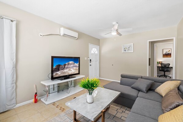 Una sala de estar con televisor, sofá, mesa de centro y ventilador de techo.