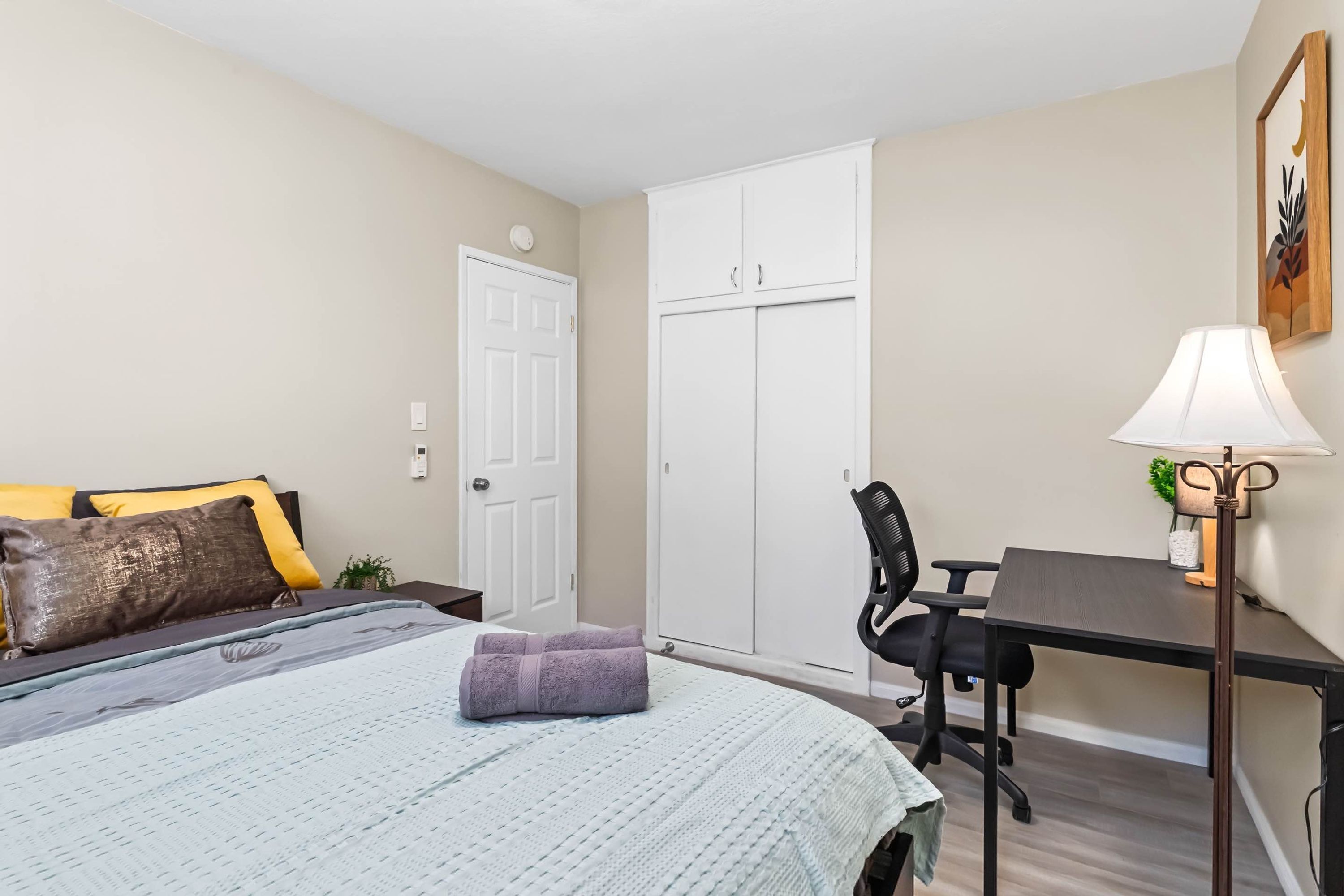 A bedroom with a bed, a desk, a chair, a wardrobe, and a lamp.