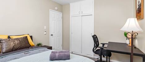 A bedroom with a bed, a desk, a chair, a wardrobe, and a lamp.