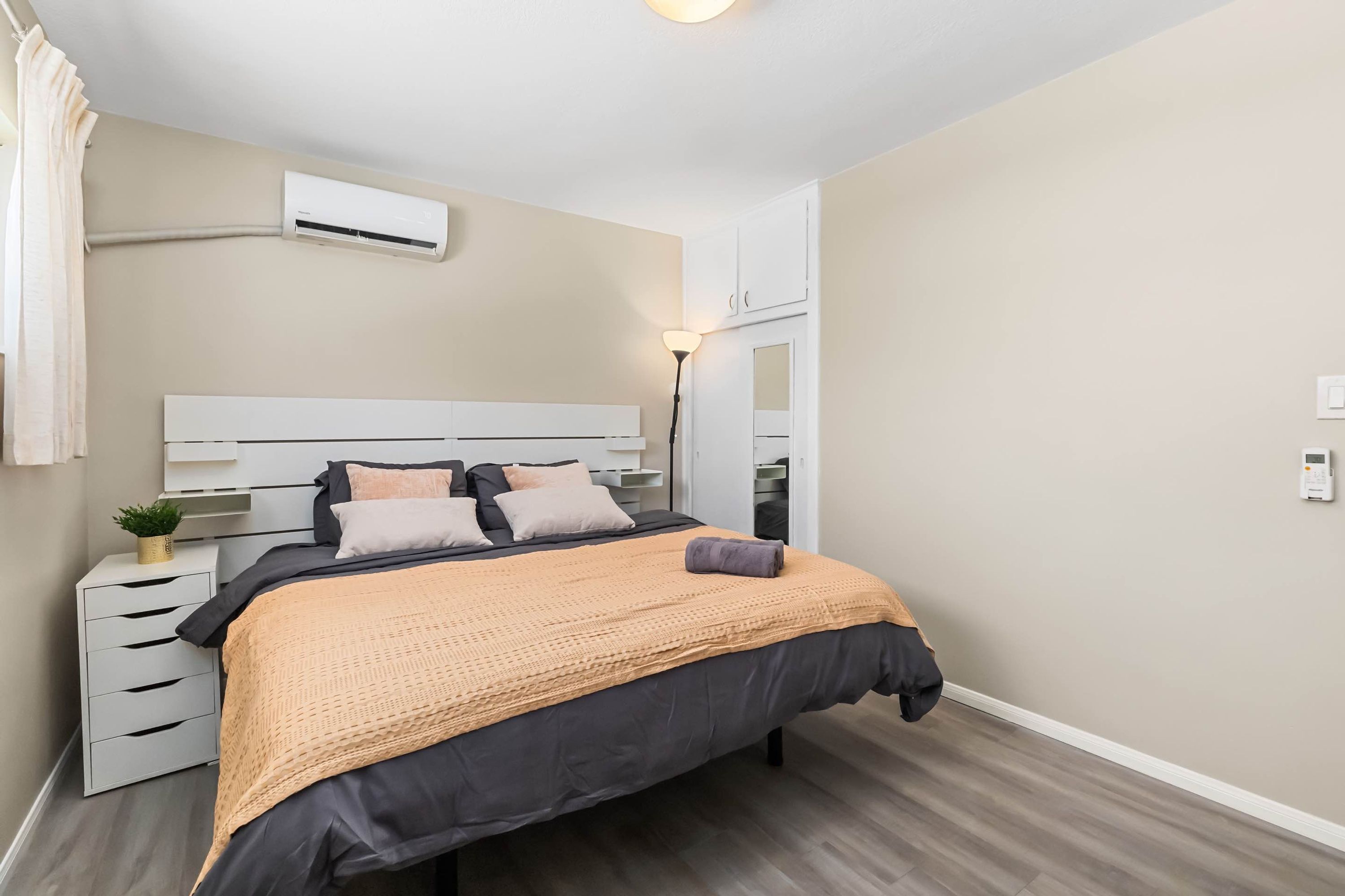 Ein modernes Schlafzimmer mit Bett, Nachttischen, einer Klimaanlage und einer Lampe.