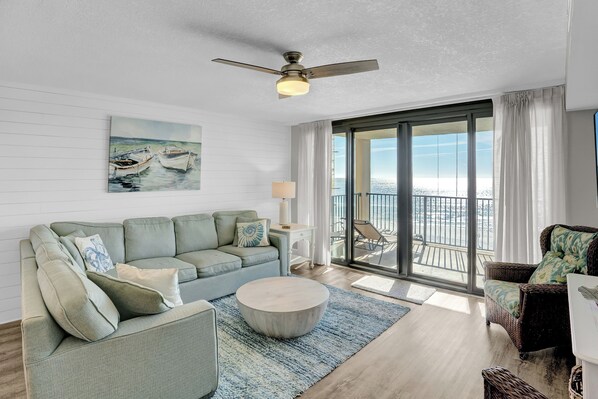 A living room with a green sofa, a round coffee table, and a painting of boats on the wall. - Wind Drift 401 by Liquid Life (Orange Beach)