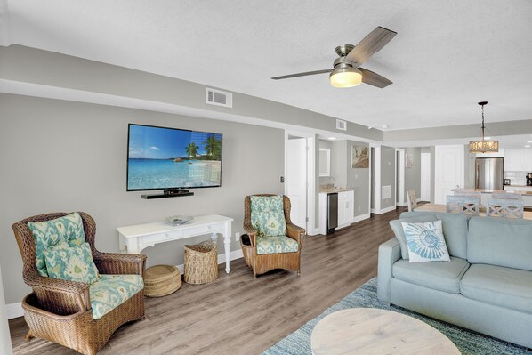 A living room with wicker chairs, a sofa, a television, and a ceiling fan.