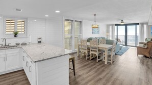 Une cuisine moderne avec des meubles blancs, un plan de travail en marbre et un coin repas comprenant une table et des chaises en bois.