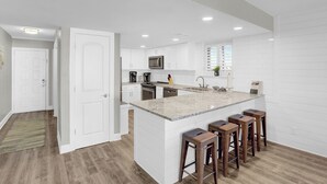Une cuisine moderne avec des meubles blancs, un grand îlot central doté de tabourets et un four à micro-ondes encastré.