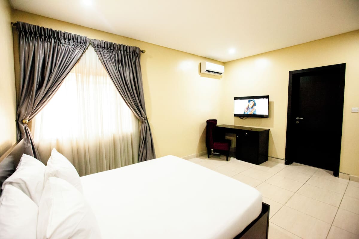 Ein Hotelzimmer mit Bett, Schreibtisch, Sessel, Fernseher und Klimaanlage.