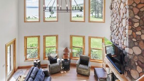 A spacious living room with a stone wall, multiple windows, a fireplace, and a television.