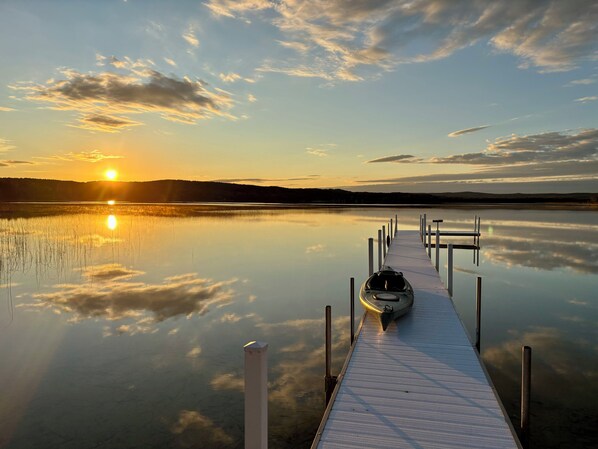 Un lago tranquilo al atardecer con un muelle que lleva a un kayak.