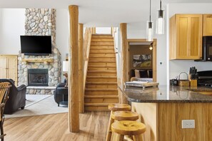 Un intérieur moderne avec une cheminée en pierre, un escalier en bois, un coin cuisine et un espace salon.