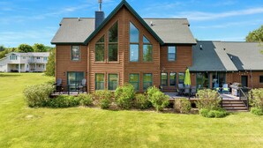 A two-story log cabin with a large deck, multiple windows, and a chimney.