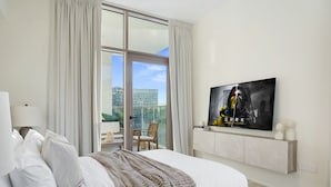 A hotel room with a large bed, a TV mounted on the wall, a balcony with a chair, and a city view. - 2BR w Canal & Burj View Near Dubai Mall (Dubai)
