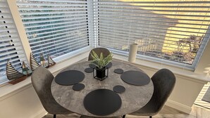 A round dining table with black circular placemats, a potted plant, and a small black stand in the center. - 2 Bedroom, Cozy Coastal Retreat in Anstruther (Anstruther)