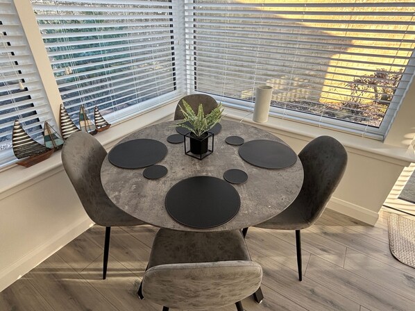 A round dining table with black circular placemats, a potted plant, and a small black stand in the center. - 2-beds, Sleeps 4 w/ Parking, 15 Mins to St Andrews (Anstruther)