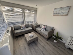 A modern living room with grey sofas, wicker furniture, a wooden coffee table, and a potted plant. - 2-beds, Sleeps 4 w/ Parking, 15 Mins to St Andrews (Anstruther)