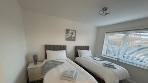 A bedroom with two beds, a nightstand, a lamp, a window with blinds, and a ceiling fan. - 2 Bedroom, Cozy Coastal Retreat in Anstruther (Anstruther)