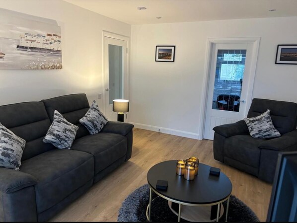 A modern living room with two dark sofas, a round coffee table, and a lamp. - 2-beds, Sleeps 4 w/ Parking, 15 Mins to St Andrews (Anstruther)
