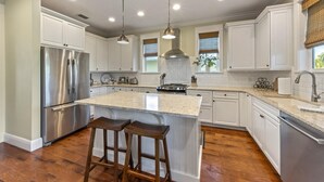 A modern kitchen with white cabinets, stainless steel appliances, a large island with bar stools, and pendant lighting. - Magnolia Cottage: Private Pool, Near Beaches & Pine Ave (Anna Maria)