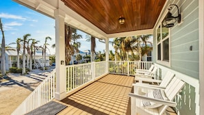 A covered porch with wooden flooring, white railings, and white outdoor furniture. - Magnolia Cottage: Private Pool, Near Beaches & Pine Ave (Anna Maria)