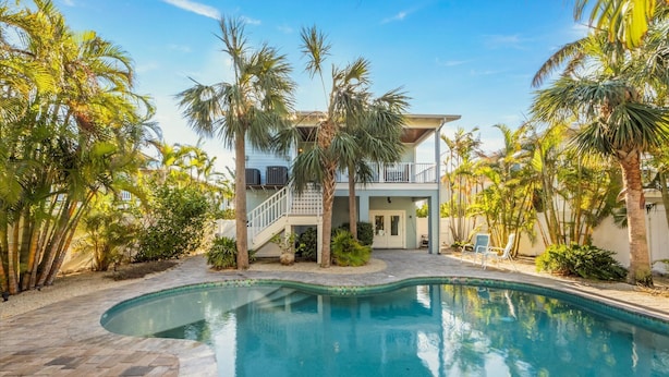A swimming pool surrounded by palm trees and a two-story house with a balcony. - Magnolia Cottage: Private Pool, Near Beaches & Pine Ave (Anna Maria)