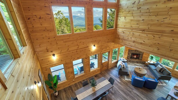 A spacious wooden cabin with multiple large windows offering mountain views, a cozy living area with sofas and a fireplace, and a dining area with a table and chairs. - Private Indoor Pool Cabin | Game Room + Firepit (Gatlinburg)