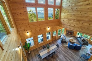 Une cabane en bois spacieuse, dotée de nombreuses grandes fenêtres offrant une vue sur les montagnes, d’un salon confortable avec des canapés et une cheminée, ainsi que d’un coin repas avec une table et des chaises.