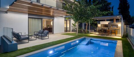 A modern house with a swimming pool, outdoor seating, and a well-maintained lawn.