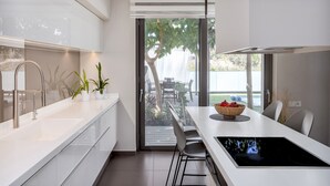 Une cuisine moderne dotée d’un îlot central, d’un coin repas avec une table et des chaises, et offrant une vue sur l’extérieur grâce à une porte vitrée.