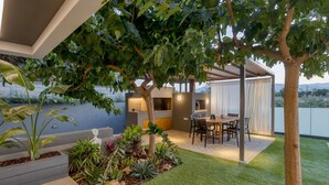 Un espace de restauration extérieur moderne, avec une table et des chaises, entouré d’une végétation luxuriante et d’un arbre.