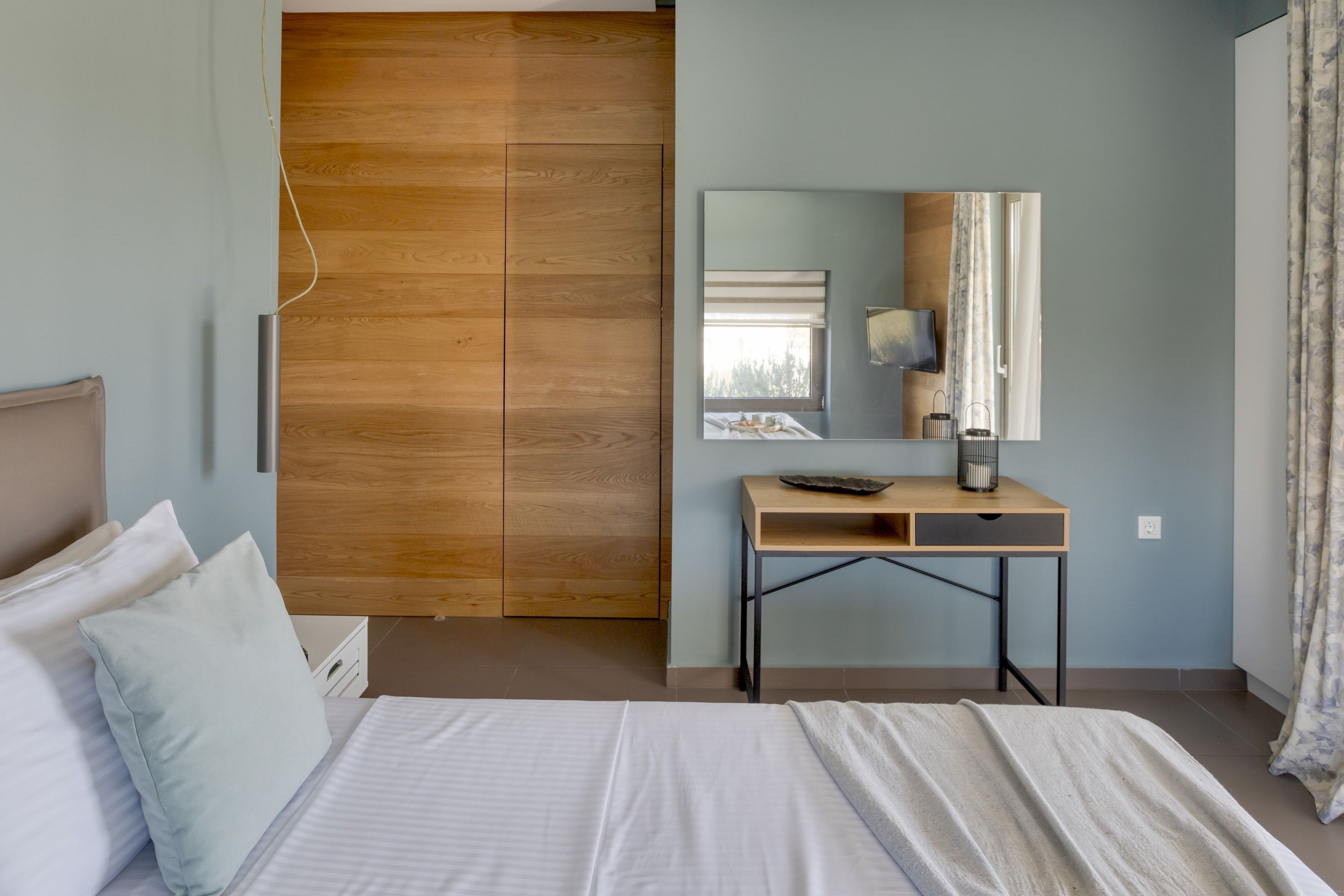 Une chambre à coucher avec un lit, une armoire en bois, un bureau avec un miroir et une fenêtre avec des rideaux.